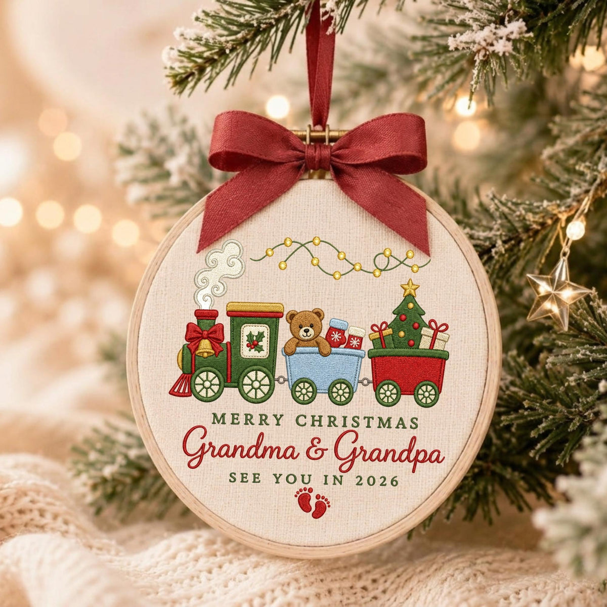 May include: A round wooden embroidery hoop ornament featuring a fabric center with an embroidered Christmas train carrying a teddy bear and tree. The text reads Merry Christmas Grandma &amp; Grandpa See You In 2026 with red baby footprints and a dark red ribbon bow.
