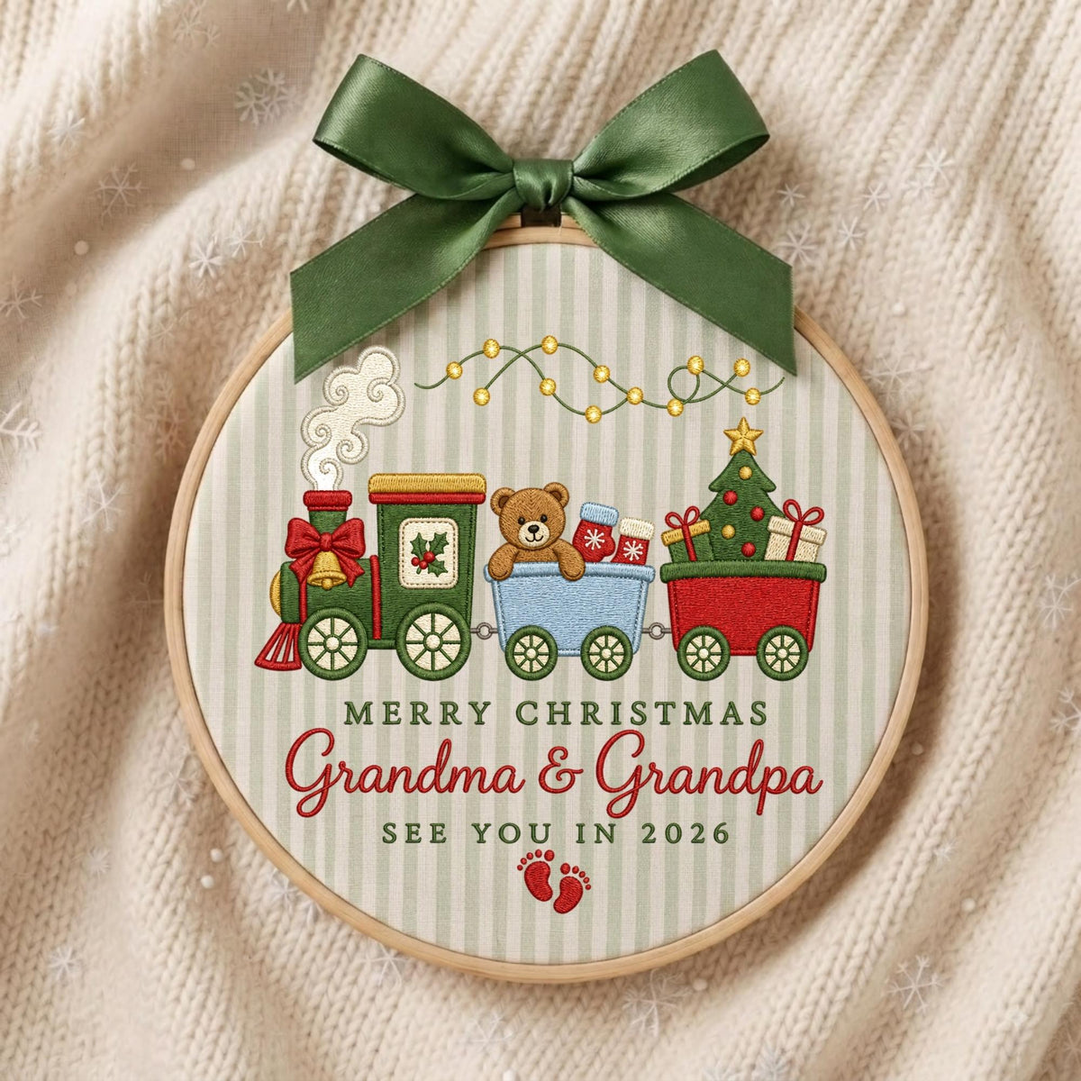 May include: A circular embroidery hoop featuring a Christmas train design with a teddy bear, gifts, and a tree. The text reads MERRY CHRISTMAS Grandma &amp; Grandpa SEE YOU IN 2026. A dark green satin ribbon bow is tied at the top of the wooden frame.