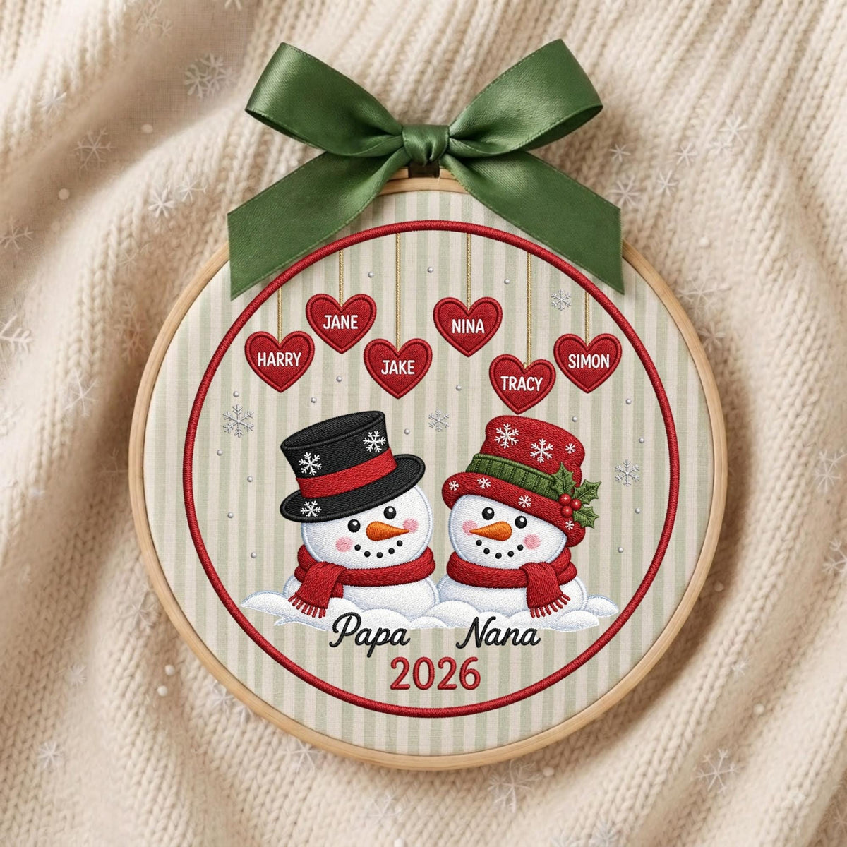 May include: A circular embroidery hoop ornament featuring two snowmen with red scarves and hats, one black and one red. Above them are six red hearts with the names Jane, Nina, Harry, Jake, Tracy, and Simon. The text reads Papa Nana 2026.