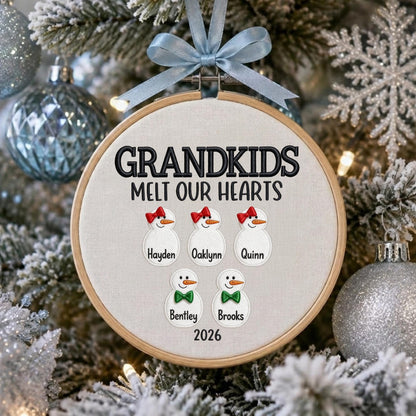 May include: A round wooden embroidery hoop ornament featuring the black embroidered text GRANDKIDS MELT OUR HEARTS and 2026. It displays five white snowman figures with orange noses, red bows, or green bow ties, labeled Hayden, Oaklynn, Quinn, Bentley, and Brooks.
