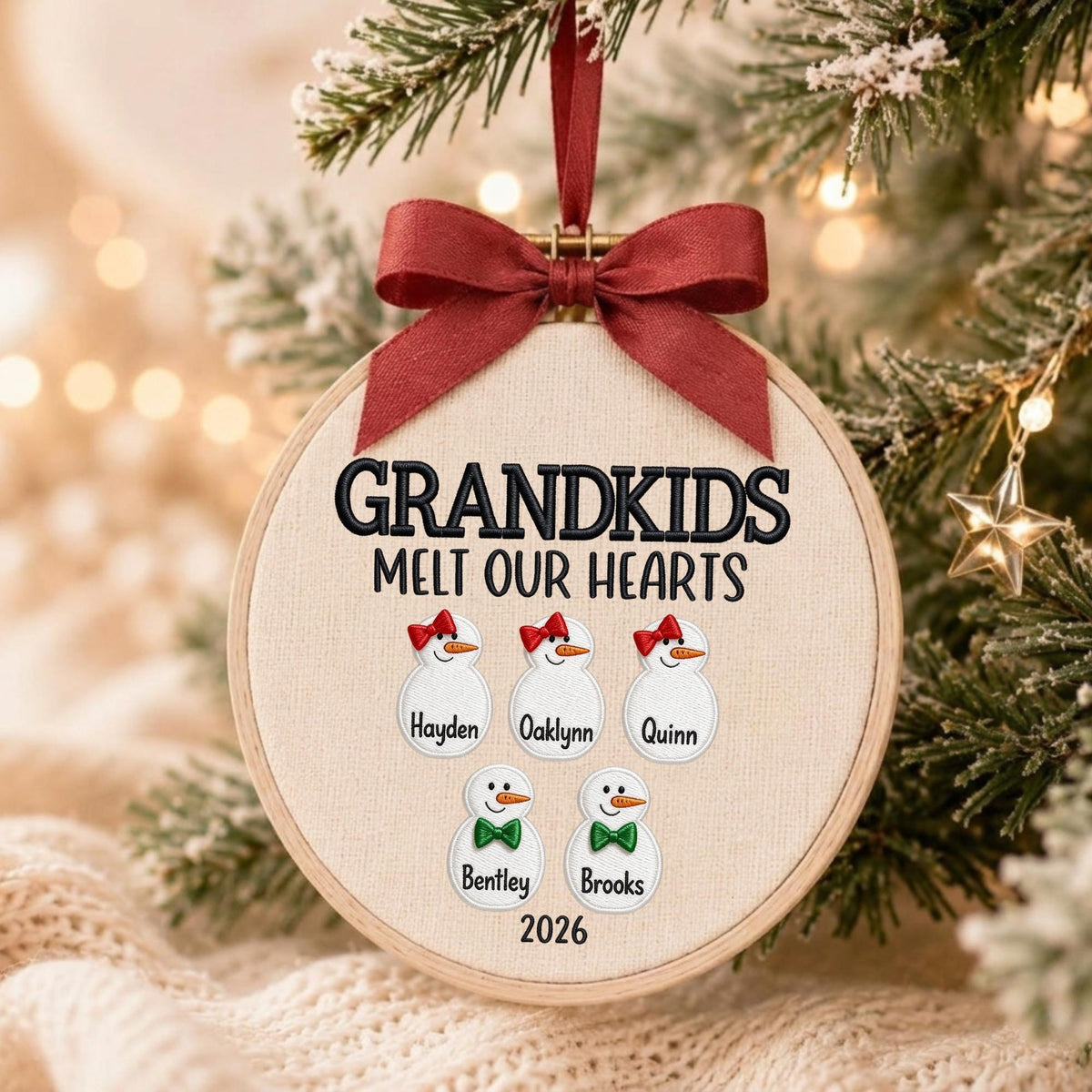 May include: A round embroidery hoop ornament featuring a cream fabric background with the embroidered text GRANDKIDS MELT OUR HEARTS. It displays five snowman figures with names Hayden, Oaklynn, Quinn, Bentley, and Brooks, topped with a red ribbon bow.