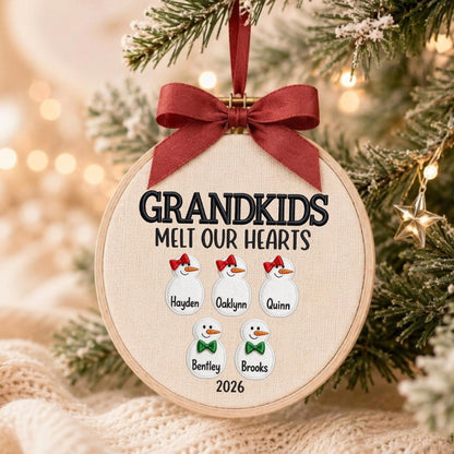 May include: A round embroidery hoop ornament featuring a cream fabric background with the embroidered text GRANDKIDS MELT OUR HEARTS. It displays five snowman figures with names Hayden, Oaklynn, Quinn, Bentley, and Brooks, topped with a red ribbon bow.
