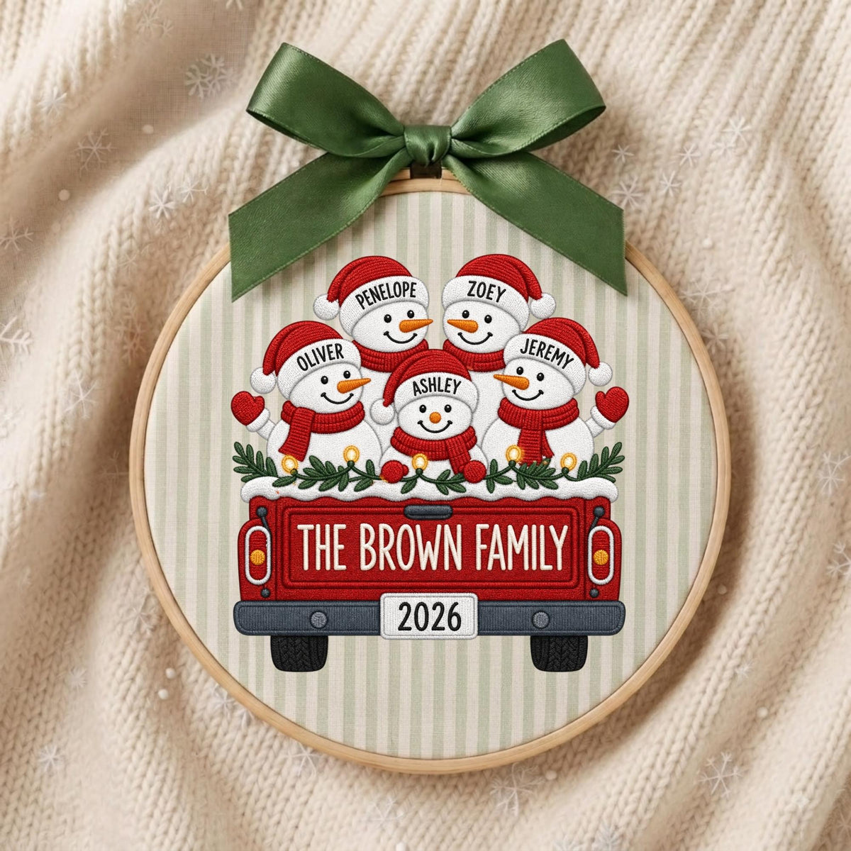 May include: A circular wooden embroidery hoop ornament featuring a red truck illustration carrying five snowmen wearing red hats and scarves. The snowmen are labeled Penelope, Zoey, Oliver, Jeremy, and Ashley. The truck reads The Brown Family 2026.