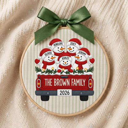May include: A circular wooden embroidery hoop ornament featuring a red truck illustration carrying five snowmen wearing red hats and scarves. The snowmen are labeled Penelope, Zoey, Oliver, Jeremy, and Ashley. The truck reads The Brown Family 2026.