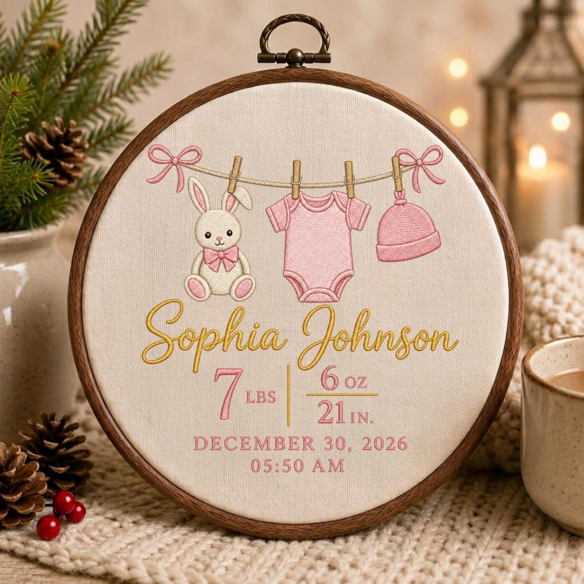 May include: A circular wooden embroidery hoop containing a cream-colored fabric with embroidered designs of a bunny, a pink onesie, and a pink hat hanging on a line. The text reads Sophia Johnson, 7 lbs 6 oz, 21 in, December 30, 2026, 05:50 AM.