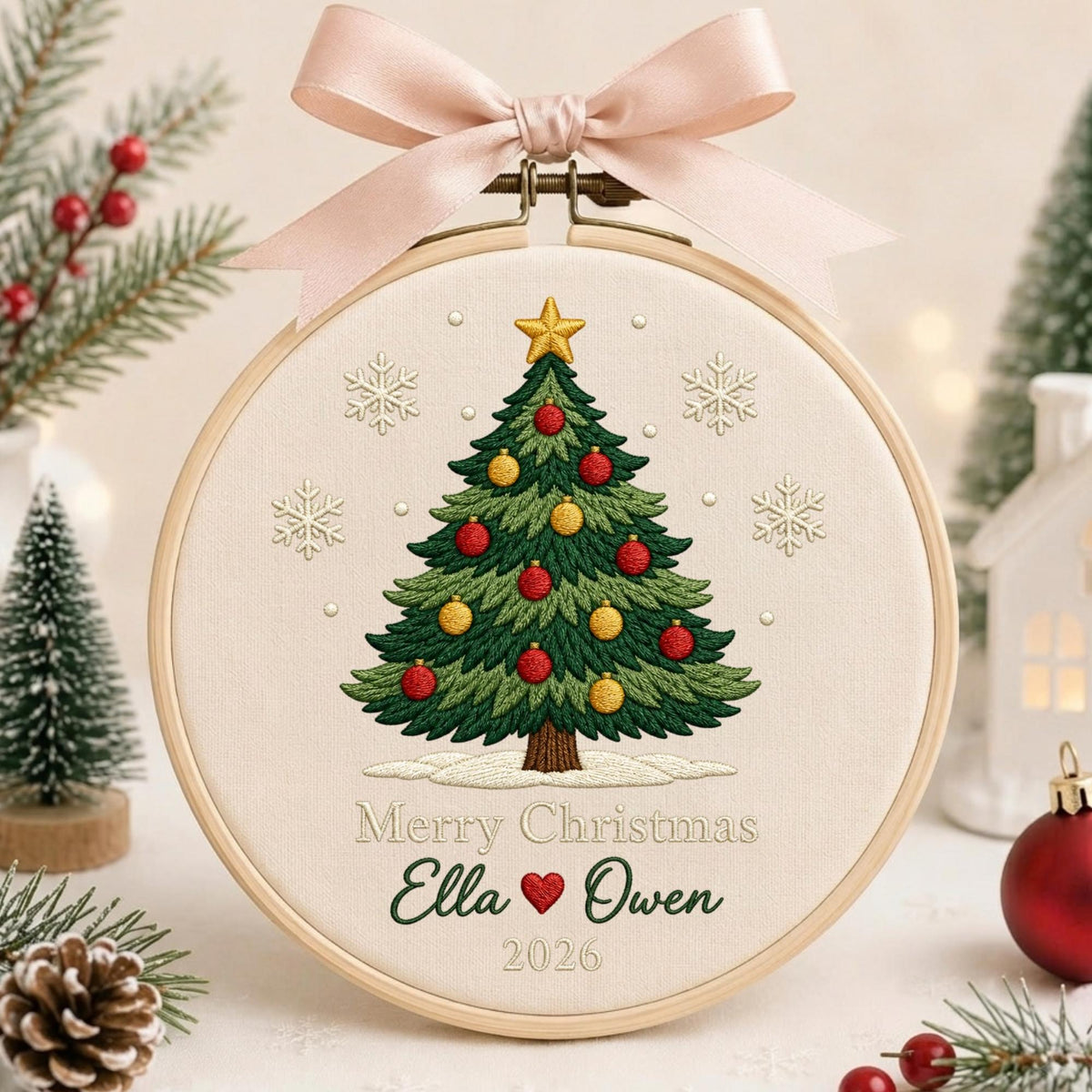 May include: A round wooden embroidery hoop containing a cream-colored fabric with a stitched green Christmas tree, red and yellow ornaments, a gold star, and white snowflakes. The text reads Merry Christmas, Ella, a heart, Owen, and 2026.