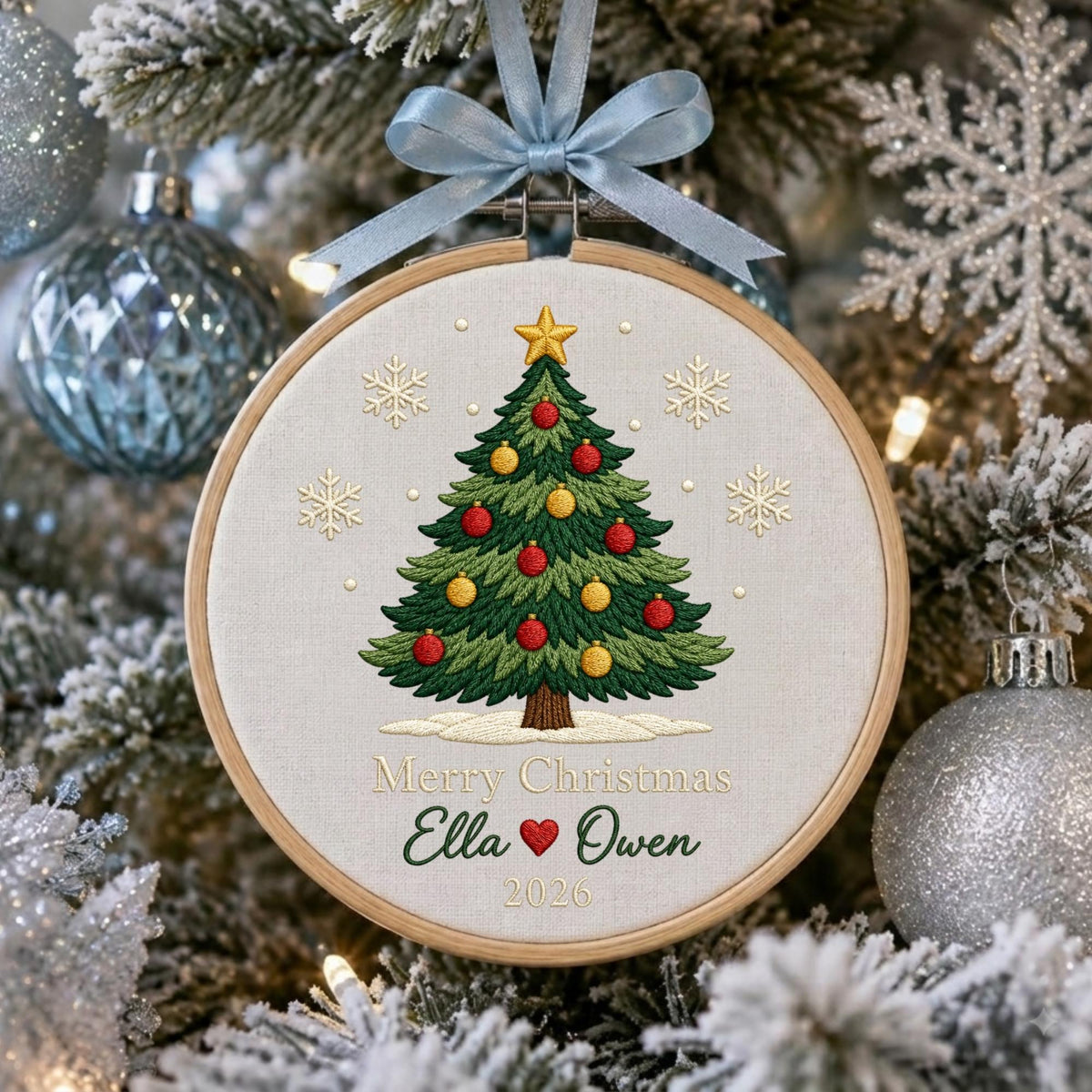 May include: A round wooden embroidery hoop ornament featuring a stitched green Christmas tree with red and yellow ornaments, a gold star topper, and white snowflakes. The text reads Merry Christmas, Ella, a red heart, Owen, and 2026.