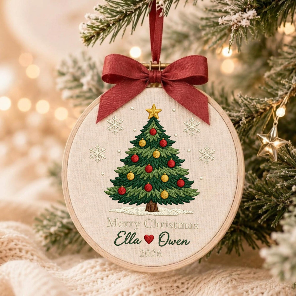 May include: A round wooden embroidery hoop ornament featuring a stitched green Christmas tree with red and yellow ornaments, a gold star topper, and white snowflakes. Below the tree, the text reads Merry Christmas Ella, a red heart, Owen, 2026.
