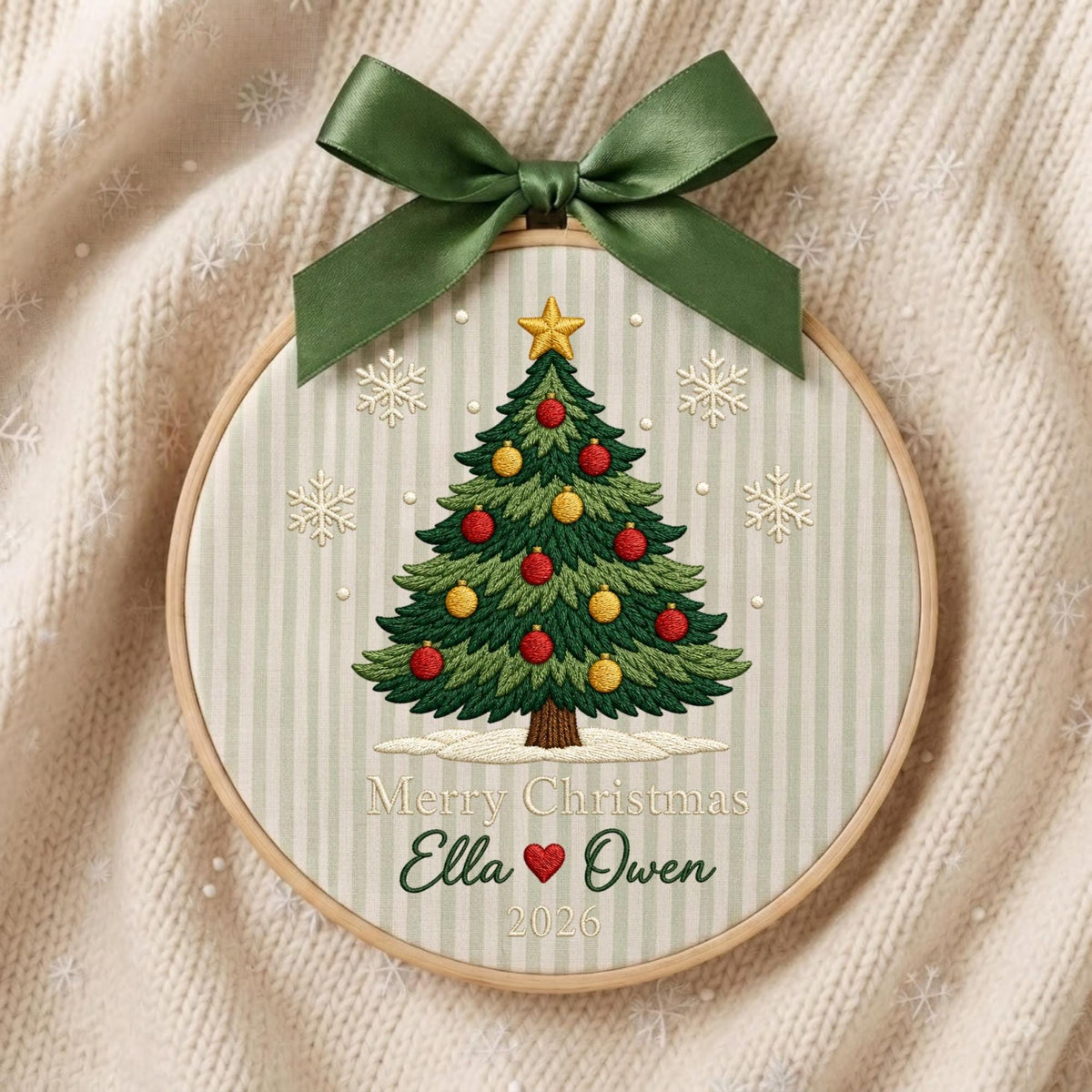 May include: A circular embroidery hoop featuring a green Christmas tree with red and yellow ornaments, topped with a gold star. The fabric has a light green striped pattern with embroidered snowflakes, the text Merry Christmas, Ella, Owen, and 2026.