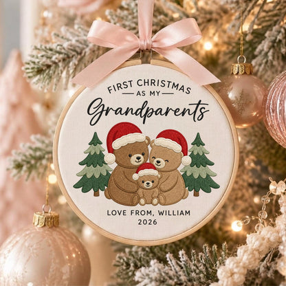 May include: A round wooden embroidery hoop ornament featuring a light fabric center with an embroidered design of three brown teddy bears wearing red Santa hats, flanked by two green pine trees. Text reads: FIRST CHRISTMAS AS MY Grandparents LOVE FROM, WILLIAM 2026.