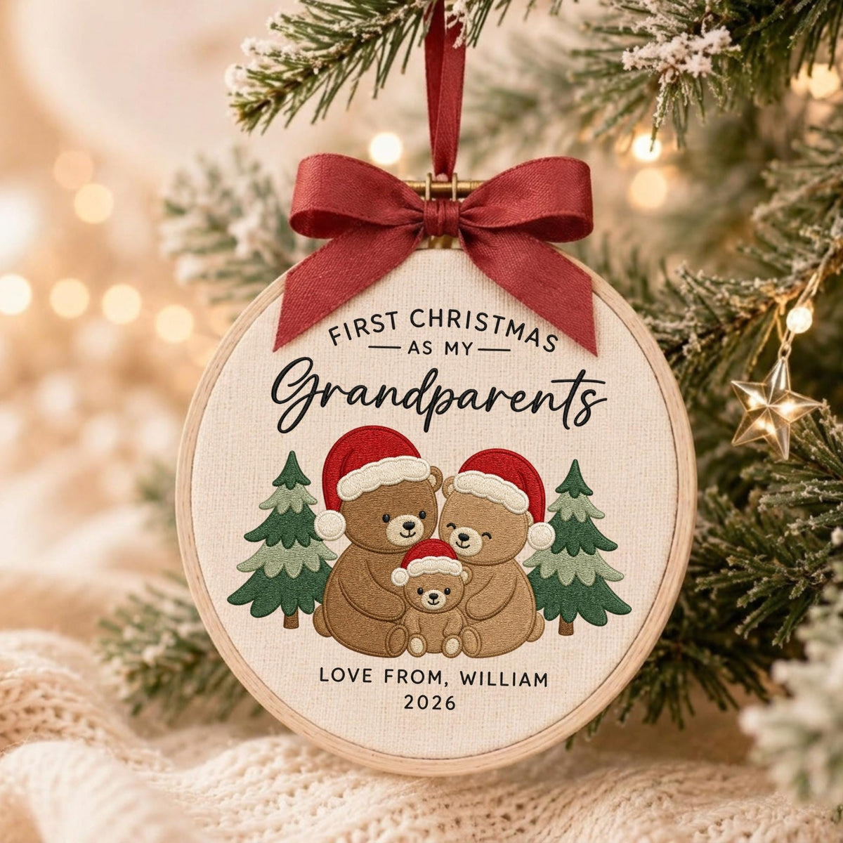May include: A round embroidery hoop ornament featuring a cream fabric background with a dark red ribbon bow at the top. The text reads FIRST CHRISTMAS AS MY Grandparents. Below, three brown bears in Santa hats stand between two green pine trees. The text LOVE FROM, WILLIAM 2026 is printed at the bottom.