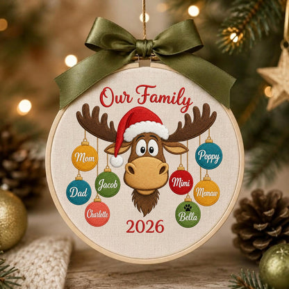 May include: A round embroidery hoop ornament featuring a brown moose wearing a red Santa hat. The text Our Family and 2026 are embroidered in red. Eight colorful ornaments hang from the moose antlers, each labeled with names: Mom, Dad, Charlotte, Jacob, Mimi, Memaw, Poppy, and Bella. An olive green ribbon bow is tied at the top.