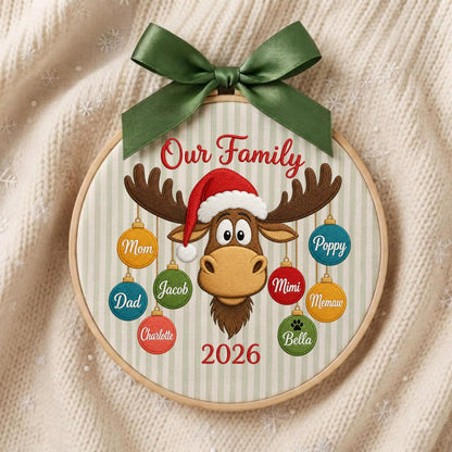May include: A round wooden embroidery hoop ornament featuring a light green and white striped fabric background. It displays a brown moose wearing a red Santa hat, surrounded by colorful hanging ornaments labeled Mom, Dad, Jacob, Charlotte, Poppy, Mimi, Memaw, and Bella. The text reads Our Family 2026, topped with a dark green satin bow.