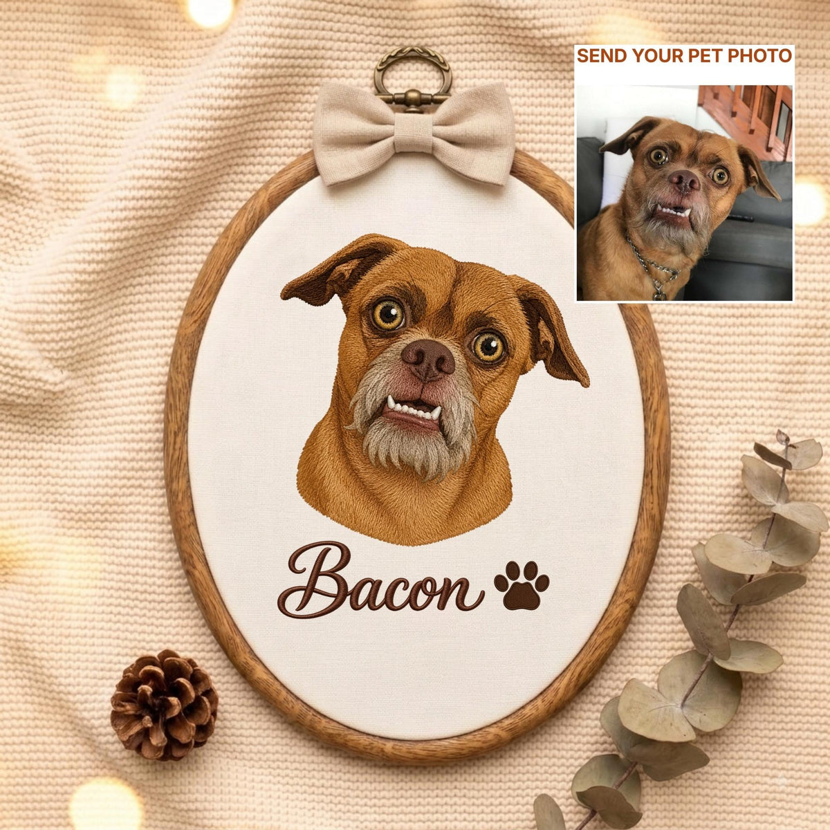May include: An oval wooden embroidery hoop containing a fabric portrait of a brown dog with a gray muzzle and visible teeth. The name Bacon is embroidered in brown script below the dog, followed by a paw print. A beige bow sits at the top.