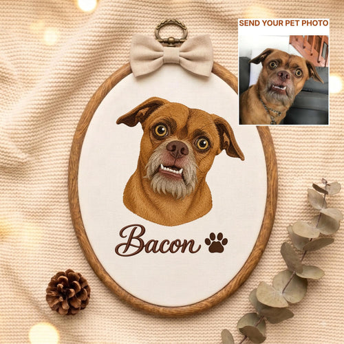 May include: An oval wooden embroidery hoop containing a fabric portrait of a brown dog with a gray muzzle and visible teeth. The name Bacon is embroidered in brown script below the dog, followed by a paw print. A beige bow sits at the top.