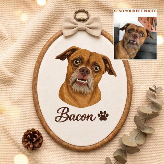 May include: An oval wooden embroidery hoop containing a fabric portrait of a brown dog with a gray muzzle and visible teeth. The name Bacon is embroidered in brown script below the dog, followed by a paw print. A beige bow sits at the top.