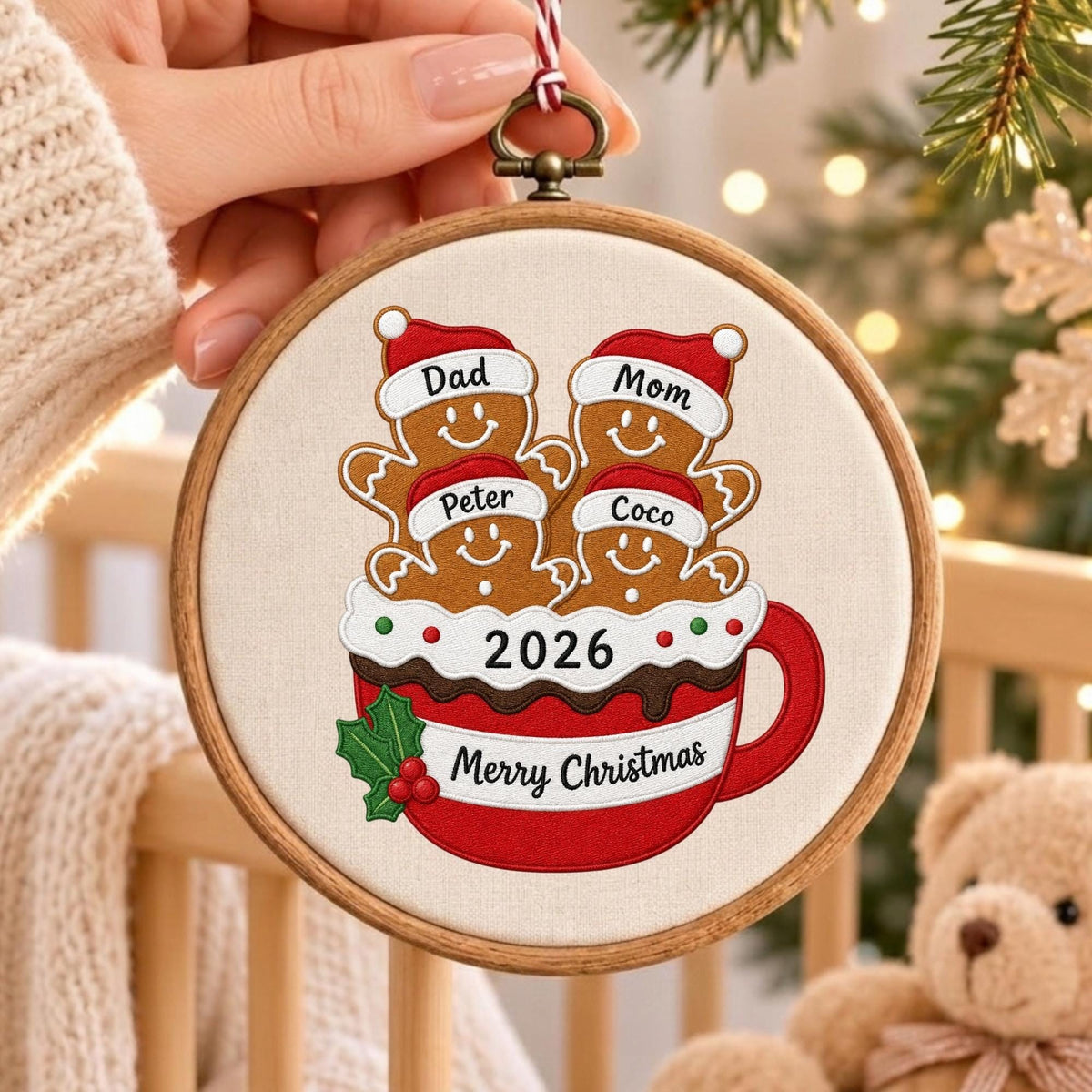 May include: A round wooden embroidery hoop ornament featuring a fabric insert with an embroidered red mug graphic. The mug contains four gingerbread figures wearing Santa hats labeled Dad, Mom, Peter, and Coco. It includes the text 2026 and Merry Christmas.
