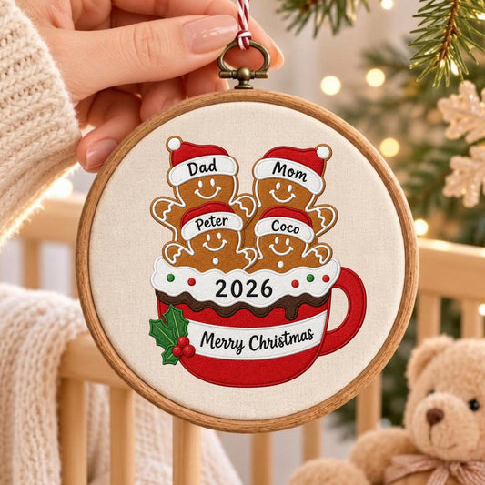 May include: A round wooden embroidery hoop ornament featuring a fabric insert with an embroidered red mug graphic. The mug contains four gingerbread figures wearing Santa hats labeled Dad, Mom, Peter, and Coco. It includes the text 2026 and Merry Christmas.