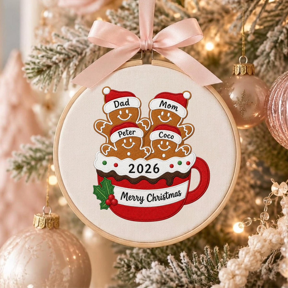 May include: A round wooden embroidery hoop ornament featuring a stitched design of four gingerbread figures in a red mug. The figures wear Santa hats labeled Dad, Mom, Peter, and Coco. The mug displays 2026 and Merry Christmas with a pink ribbon.