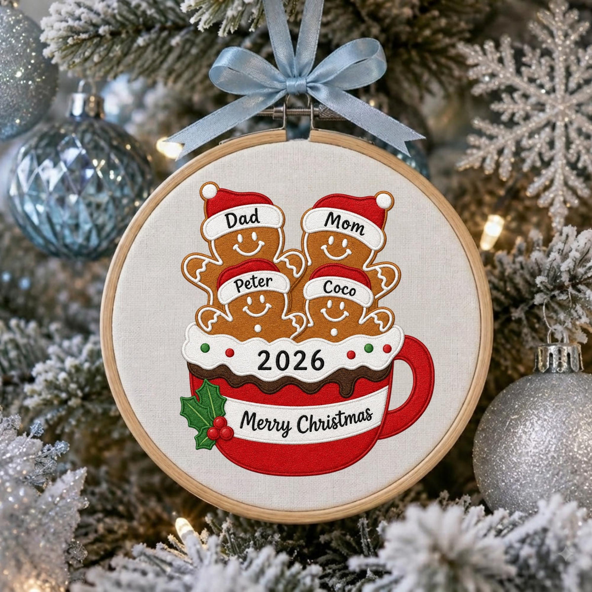 May include: A round wooden embroidery hoop ornament featuring a red mug filled with four gingerbread cookies wearing Santa hats labeled Dad, Mom, Peter, and Coco. The mug displays the text 2026 and Merry Christmas with a light blue ribbon.