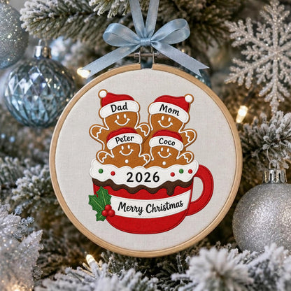 May include: A round wooden embroidery hoop ornament featuring a red mug filled with four gingerbread cookies wearing Santa hats labeled Dad, Mom, Peter, and Coco. The mug displays the text 2026 and Merry Christmas with a light blue ribbon.