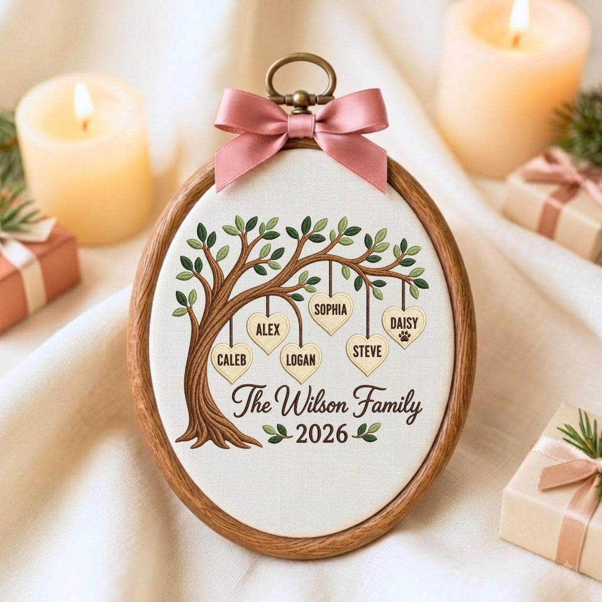 May include: An oval wooden embroidery hoop frame containing white fabric with an embroidered tree. Six heart-shaped ornaments hang from the branches, each inscribed with a name: Caleb, Alex, Logan, Sophia, Steve, and Daisy. Text reads The Wilson Family 2026.