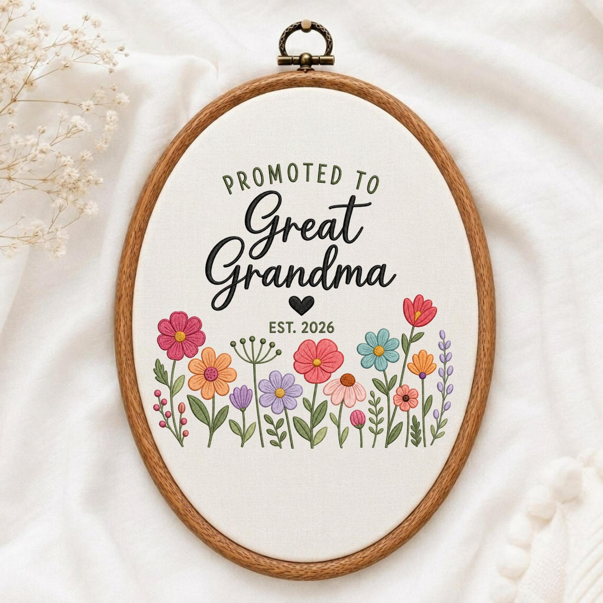 May include: An oval wooden embroidery hoop containing white fabric with the embroidered text PROMOTED TO Great Grandma, a small black heart, and the text EST. 2026, surrounded by a colorful array of embroidered wildflowers in pink, orange, blue, and purple.