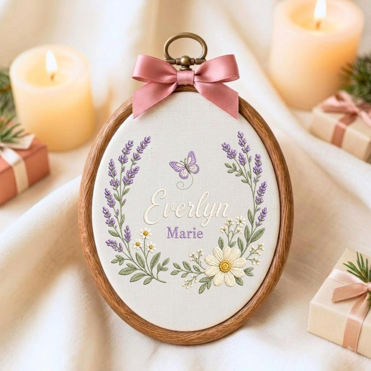 May include: An oval wooden embroidery hoop containing white fabric with a hand-stitched design of lavender sprigs, a small purple butterfly, and white daisies. The names Everlyn and Marie are embroidered in the center, topped with a pink satin bow.