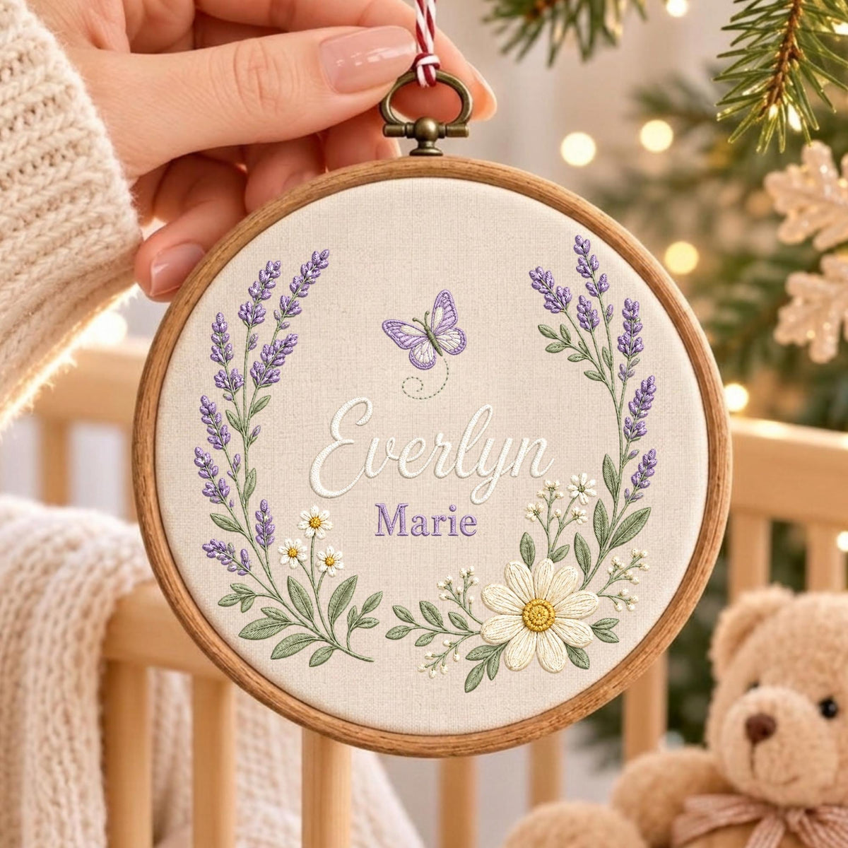 May include: A circular wooden embroidery hoop containing off-white fabric with hand-stitched lavender sprigs, white daisies, and a purple butterfly. The name Everlyn Marie is embroidered in the center in white and purple script and block lettering.