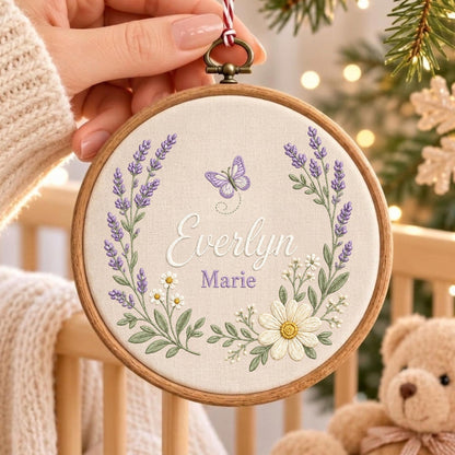 May include: A circular wooden embroidery hoop containing off-white fabric with hand-stitched lavender sprigs, white daisies, and a purple butterfly. The name Everlyn Marie is embroidered in the center in white and purple script and block lettering.