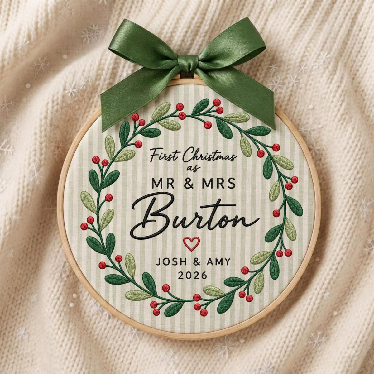 May include: A circular embroidery hoop ornament featuring a green satin bow at the top. The fabric has vertical light stripes and an embroidered wreath of green leaves and red berries. Text reads: First Christmas as MR &amp; MRS Burton, JOSH &amp; AMY, 2026.
