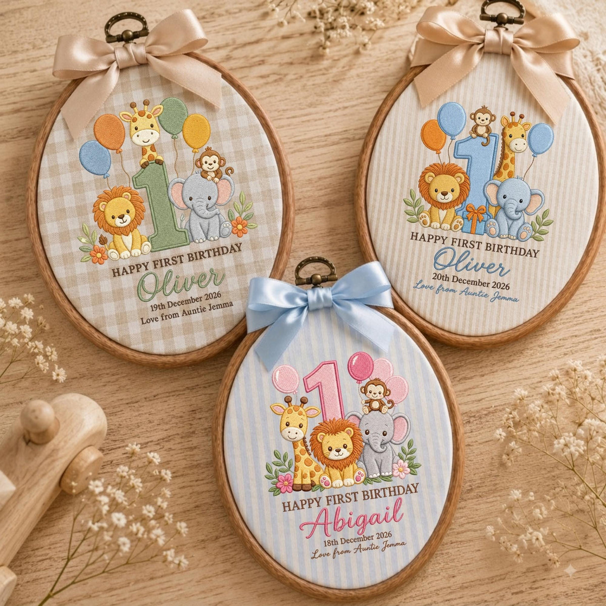 May include: Three oval embroidery hoops featuring fabric with printed illustrations of a giraffe, lion, monkey, and elephant with balloons and the number 1. Each hoop is topped with a satin ribbon bow and displays personalized birthday text.