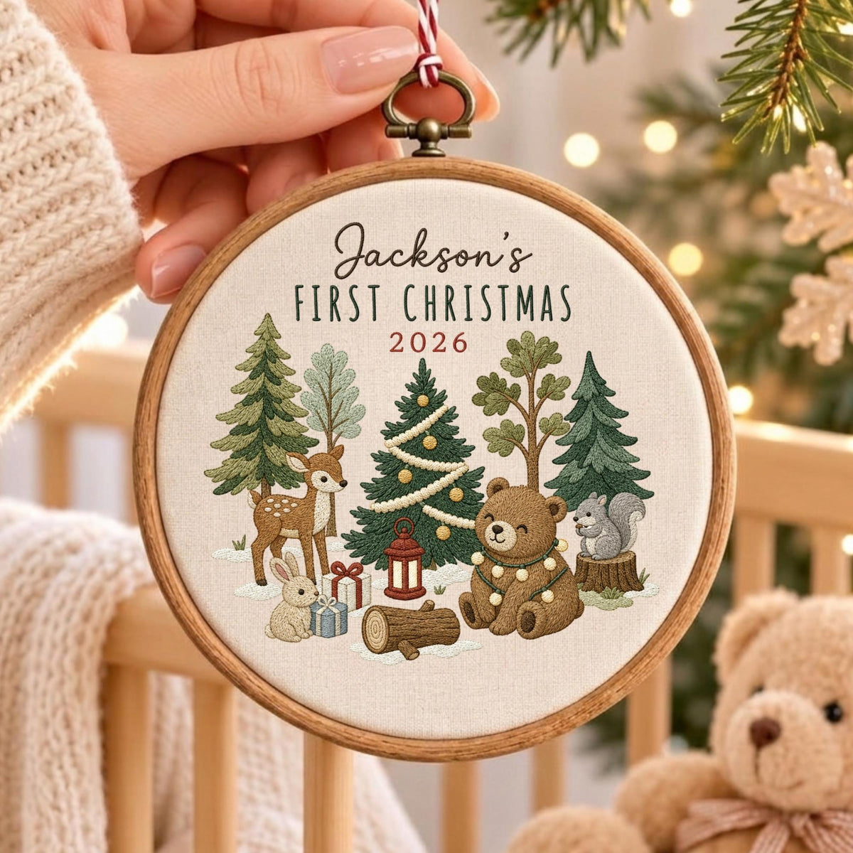 May include: A round wooden embroidery hoop ornament featuring cream fabric with embroidered forest animals, trees, and gifts. The text reads Jackson's FIRST CHRISTMAS 2026. The design includes a deer, a bear, a rabbit, and a squirrel in a snowy scene.