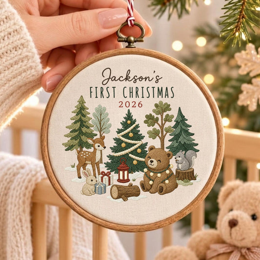 May include: A round wooden embroidery hoop ornament featuring cream fabric with embroidered forest animals, trees, and gifts. The text reads Jackson's FIRST CHRISTMAS 2026. The design includes a deer, a bear, a rabbit, and a squirrel in a snowy scene.