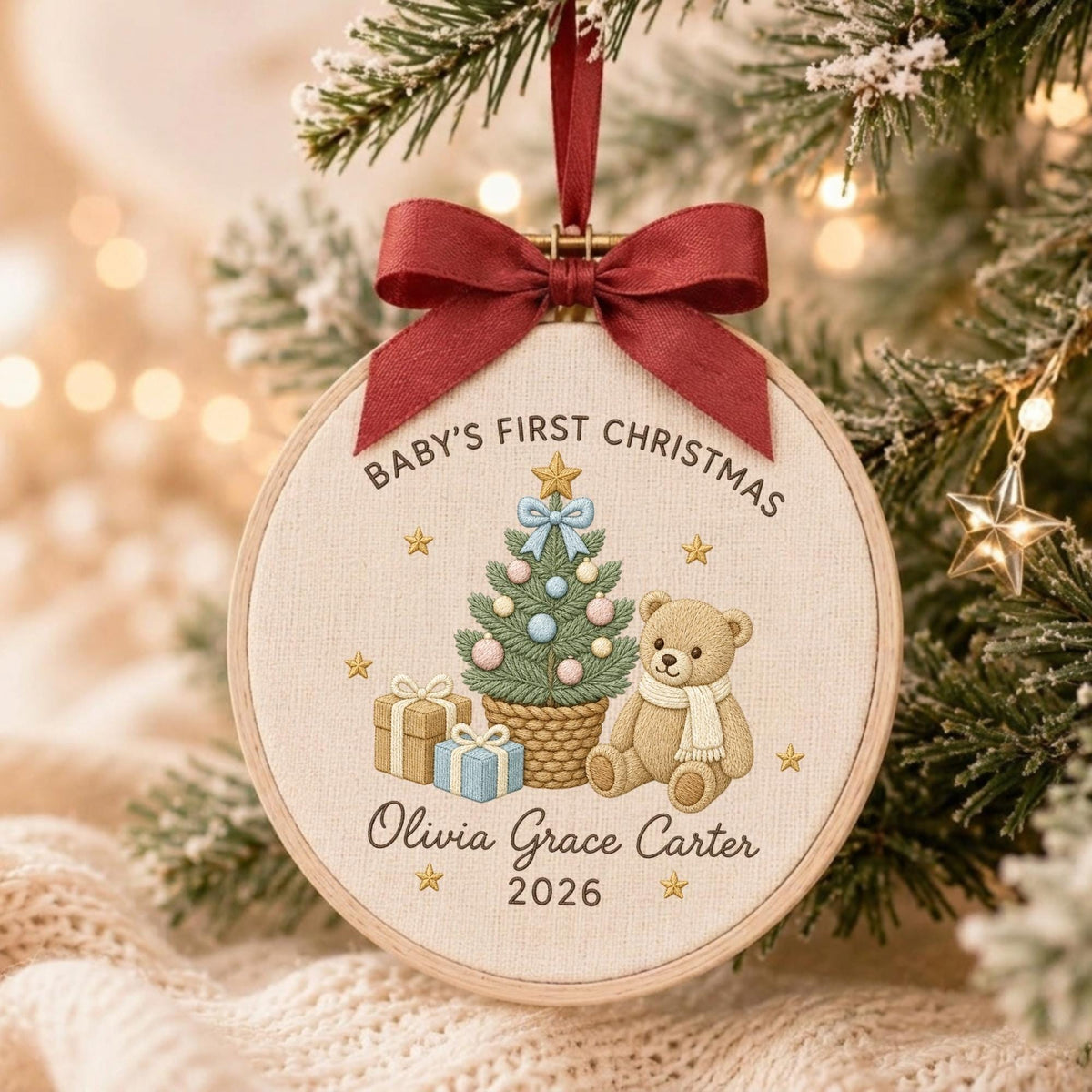 May include: A round wooden embroidery hoop ornament featuring a cream fabric center with the text Baby's First Christmas, Olivia Grace Carter, and 2026. The design includes a decorated Christmas tree, a teddy bear, and gifts, topped with a red ribbon.