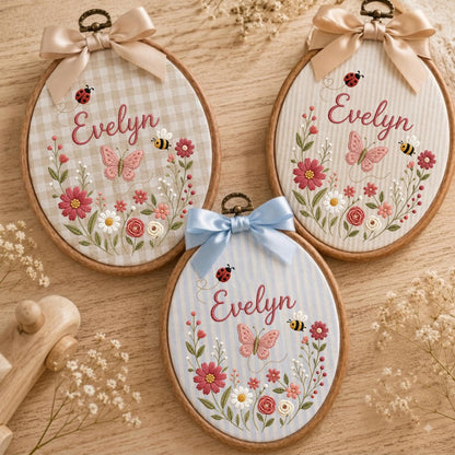 May include: Three oval embroidery hoops featuring fabric backgrounds in beige gingham, cream stripes, and light blue stripes. Each hoop displays the name Evelyn in cursive, surrounded by embroidered flowers, a butterfly, a bee, and a ladybug.