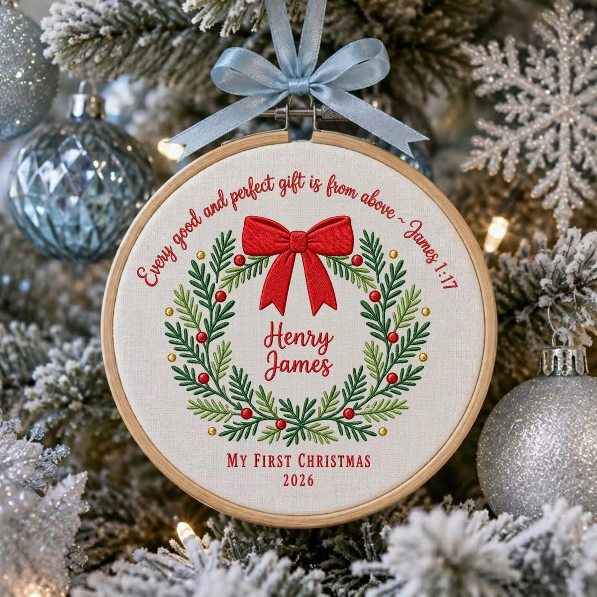 May include: A round wooden embroidery hoop ornament featuring a white fabric center with an embroidered green wreath, red berries, and a red bow. The text reads: Every good and perfect gift is from above ~ James 1:17, Henry James, My First Christmas 2026.