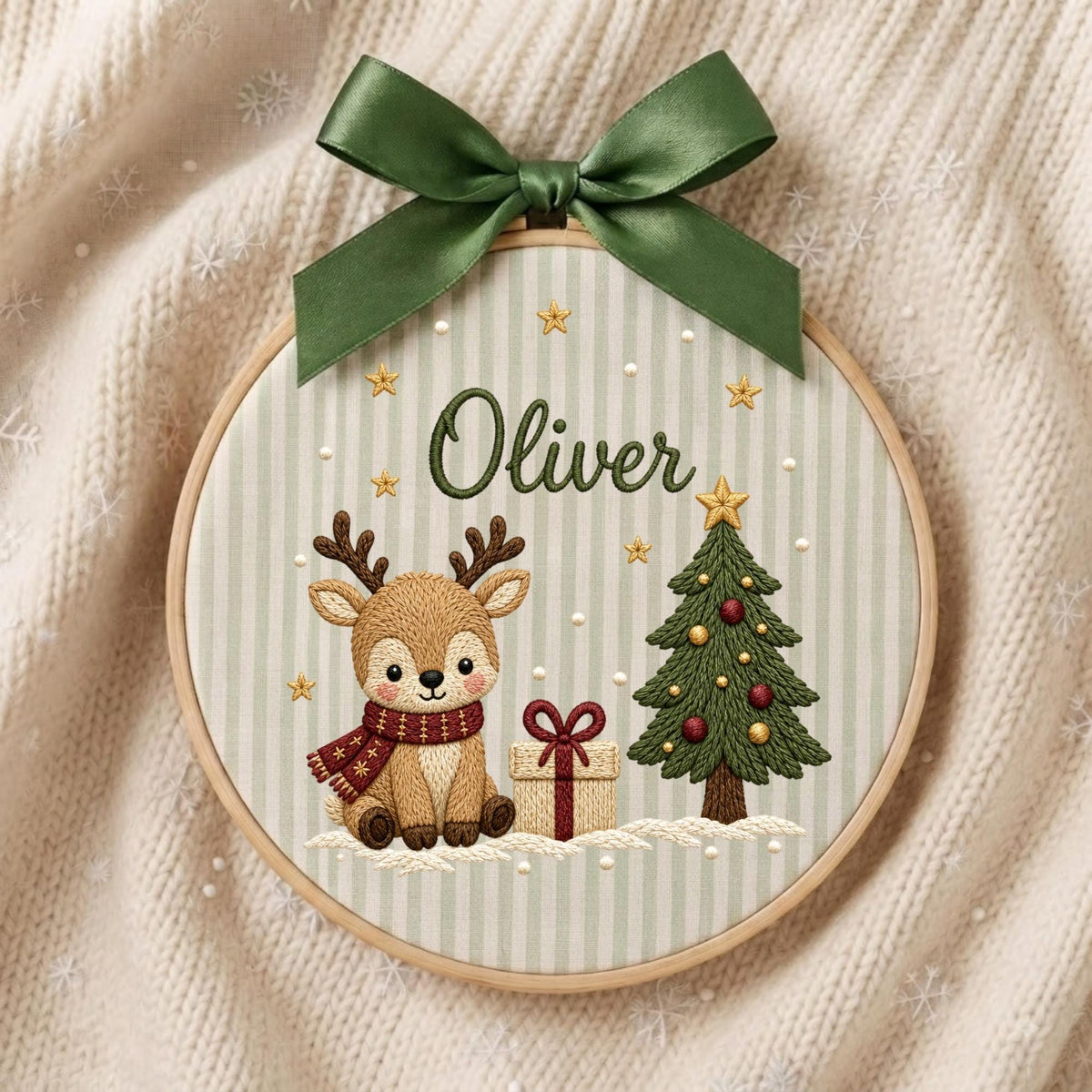 May include: A circular wooden embroidery hoop featuring a light green and white striped fabric background. The embroidery depicts a brown reindeer wearing a red scarf, a Christmas tree, a gift box, and the name Oliver in dark green script.