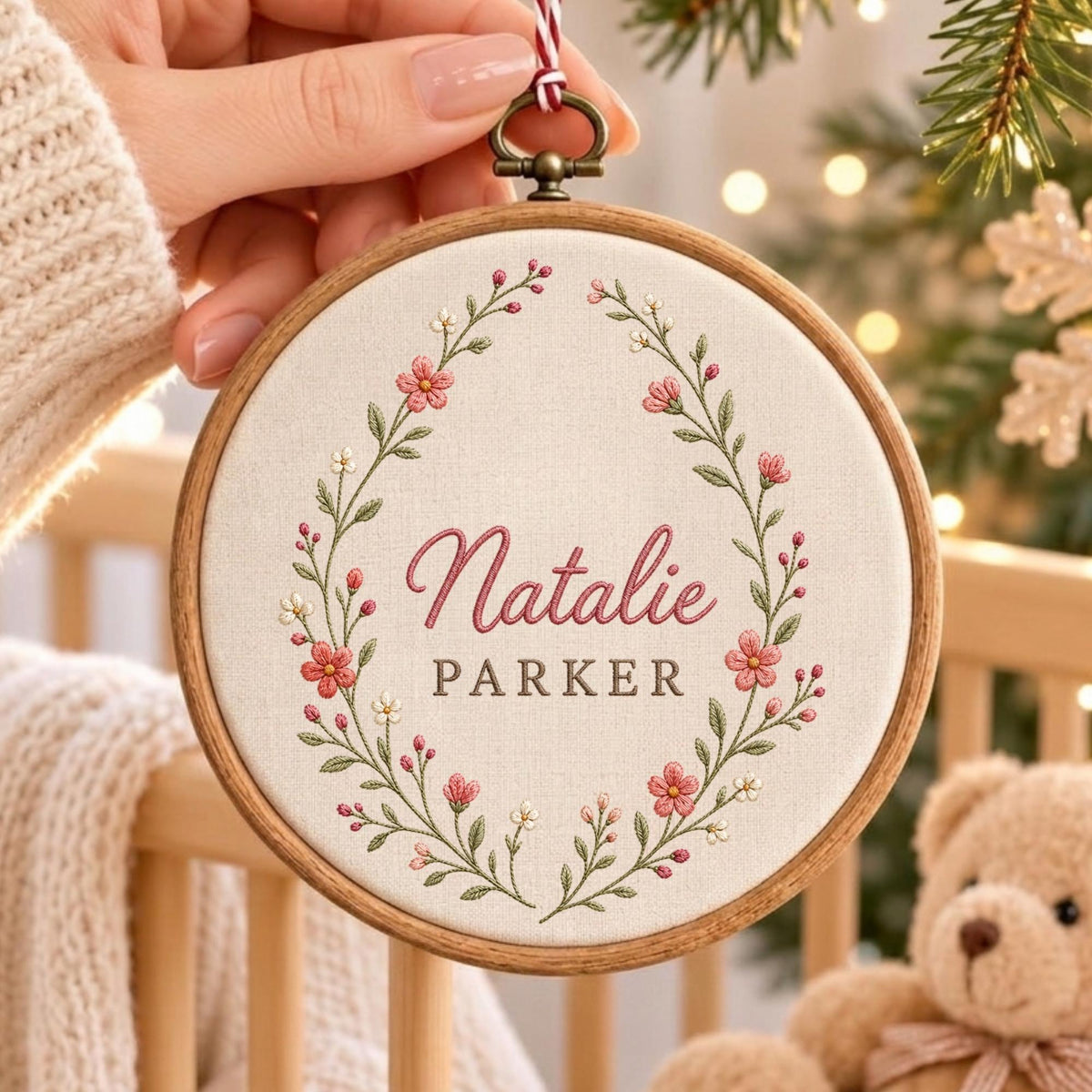 May include: A circular wooden embroidery hoop containing off-white fabric with a floral wreath design embroidered in pink and green thread. The name Natalie Parker is stitched in the center in pink cursive and dark gray block lettering.