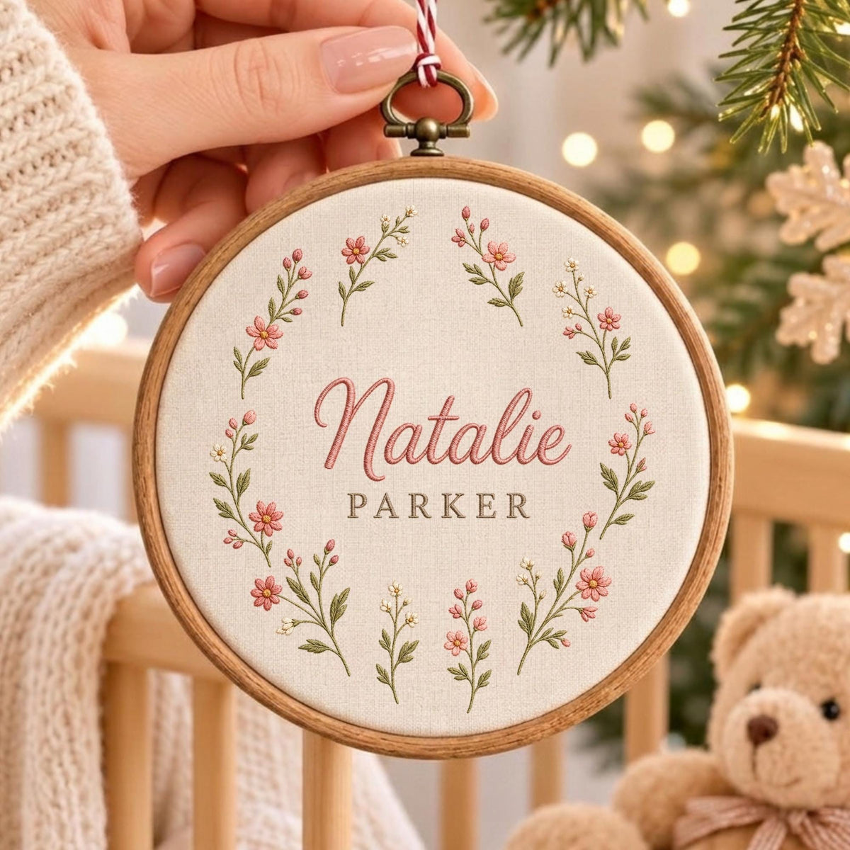 May include: A circular wooden embroidery hoop containing off-white fabric with a floral wreath design embroidered in pink and green thread. The name Natalie Parker is stitched in the center in pink and grey script and block lettering.