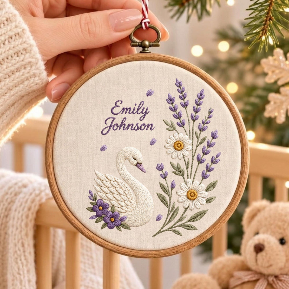 May include: A circular wooden embroidery hoop containing a white fabric panel with a hand-stitched design. The embroidery features a white swan, purple and white flowers, green leaves, and the text Emily Johnson in a purple cursive script font.