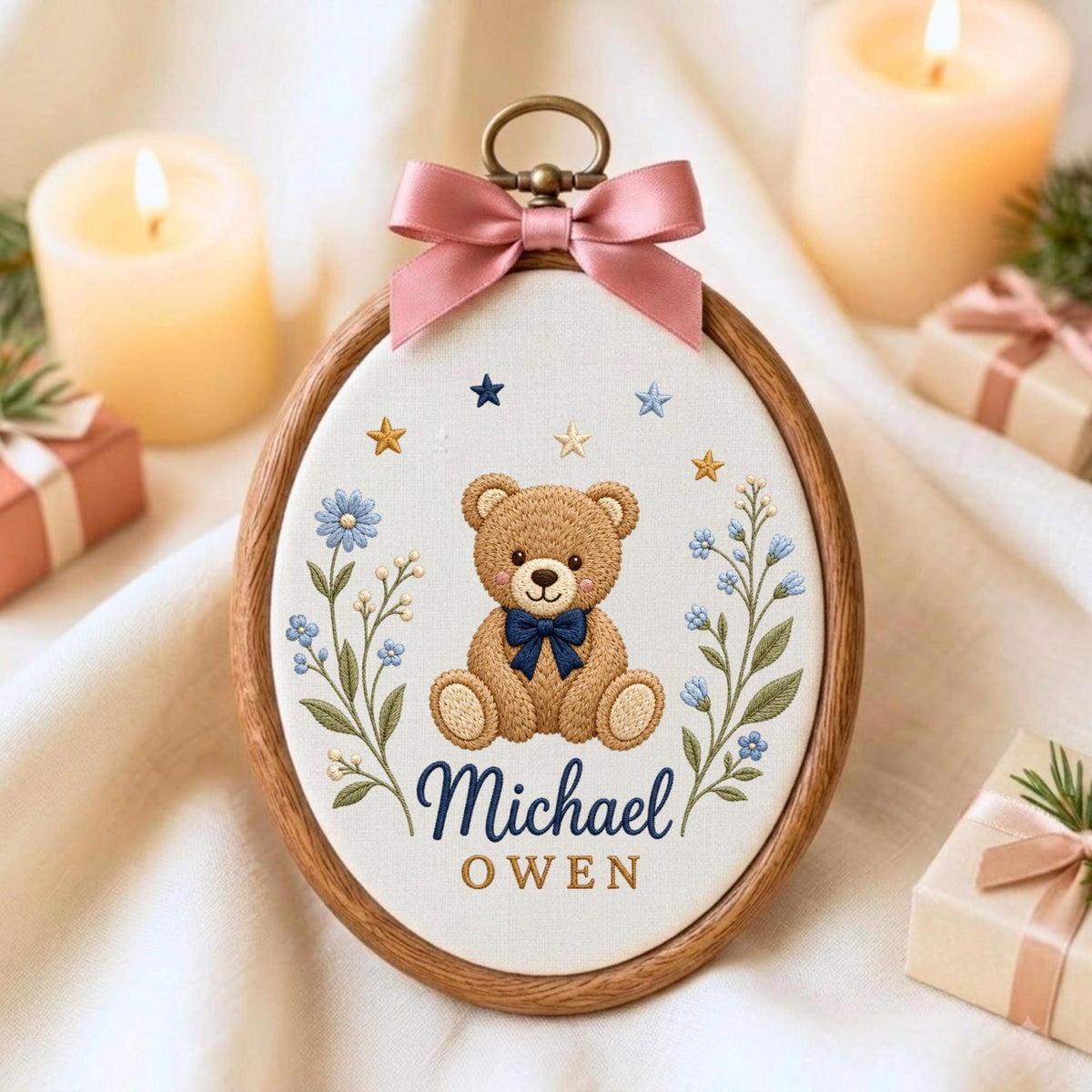 May include: An oval wooden embroidery hoop containing fabric with a stitched brown teddy bear wearing a dark blue bow tie, flanked by blue floral sprigs and small stars. The name Michael Owen is embroidered below in blue and gold script.
