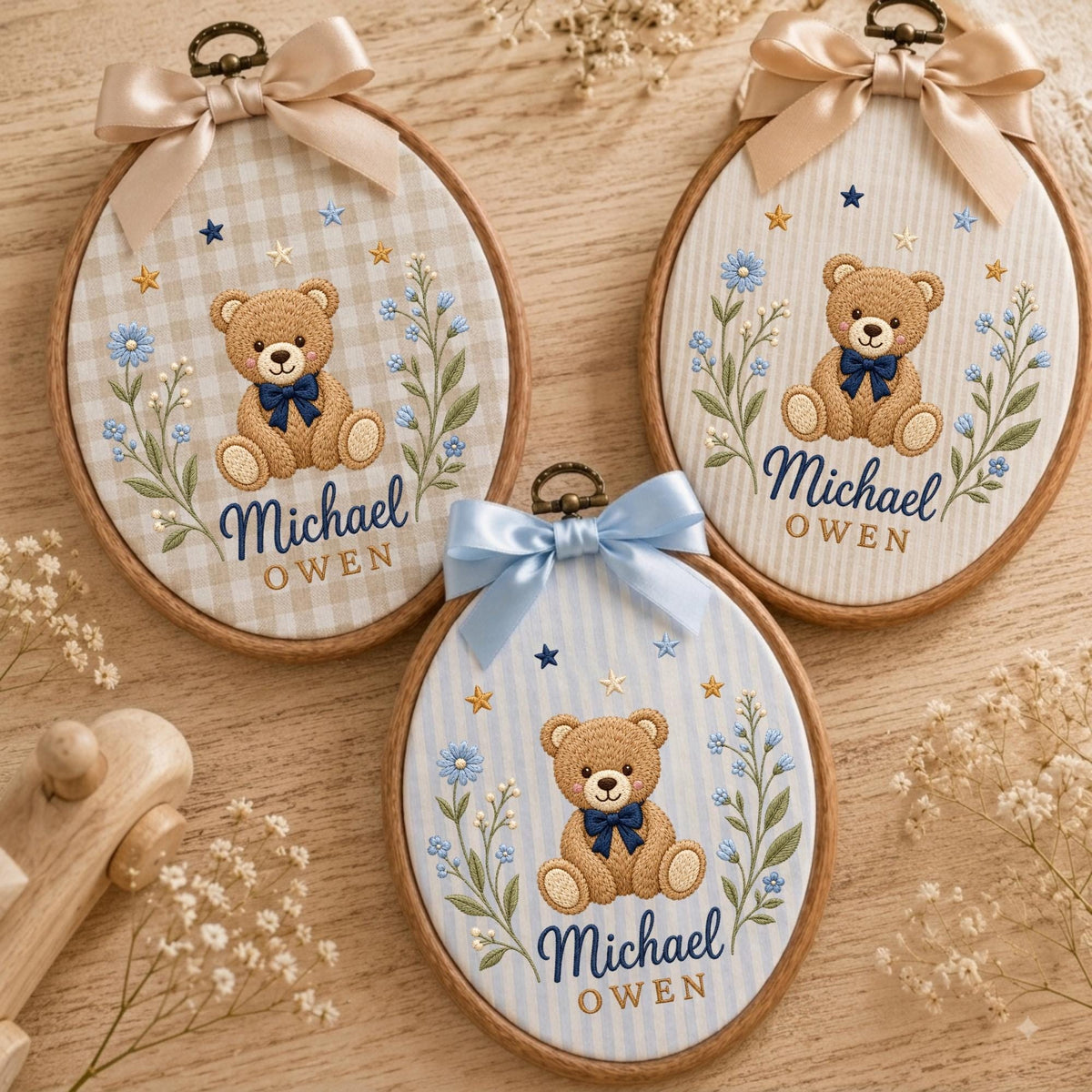 May include: Three oval wooden embroidery hoops featuring fabric backgrounds with embroidered teddy bears, blue flowers, and gold stars. Each hoop displays the name Michael Owen in dark blue and gold text, topped with a decorative satin ribbon bow.