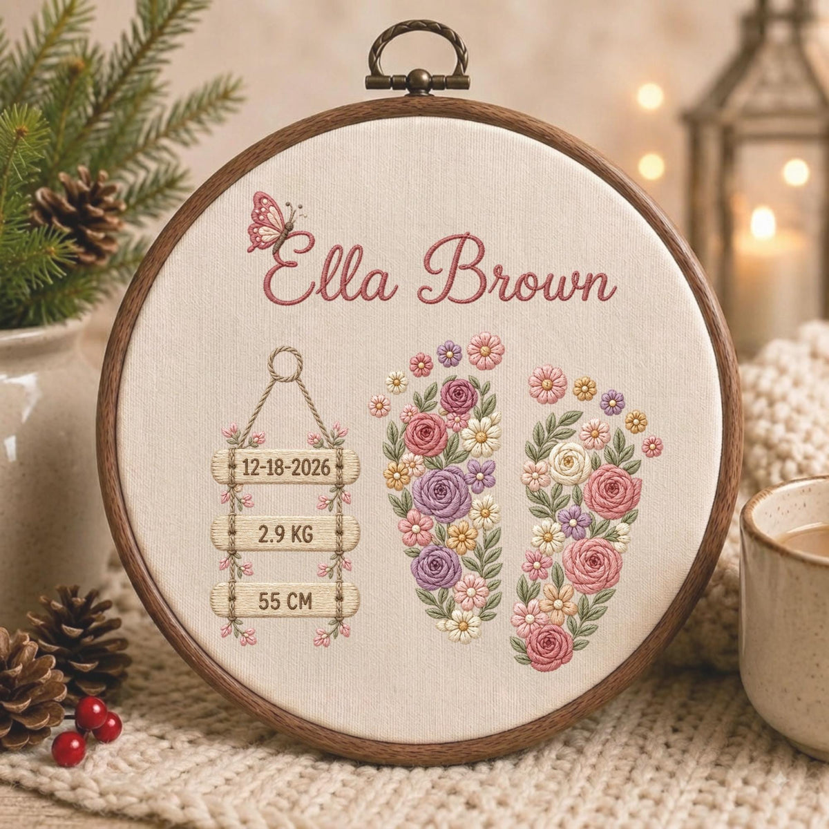 May include: A circular wooden embroidery hoop containing cream fabric with a hand-stitched design. The embroidery features the name Ella Brown, a small butterfly, two floral-filled baby footprints, and three hanging wooden signs reading 12-18-2026, 2.9 KG, and 55 CM.