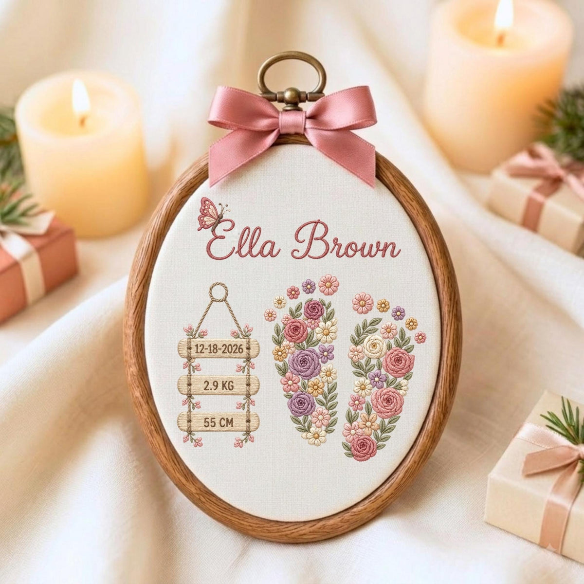 May include: An oval wooden embroidery hoop containing white fabric with floral-patterned baby footprints, a butterfly, and the text Ella Brown. Three hanging wooden signs display 12-18-2026, 2.9 KG, and 55 CM. A pink satin bow is attached to the top.