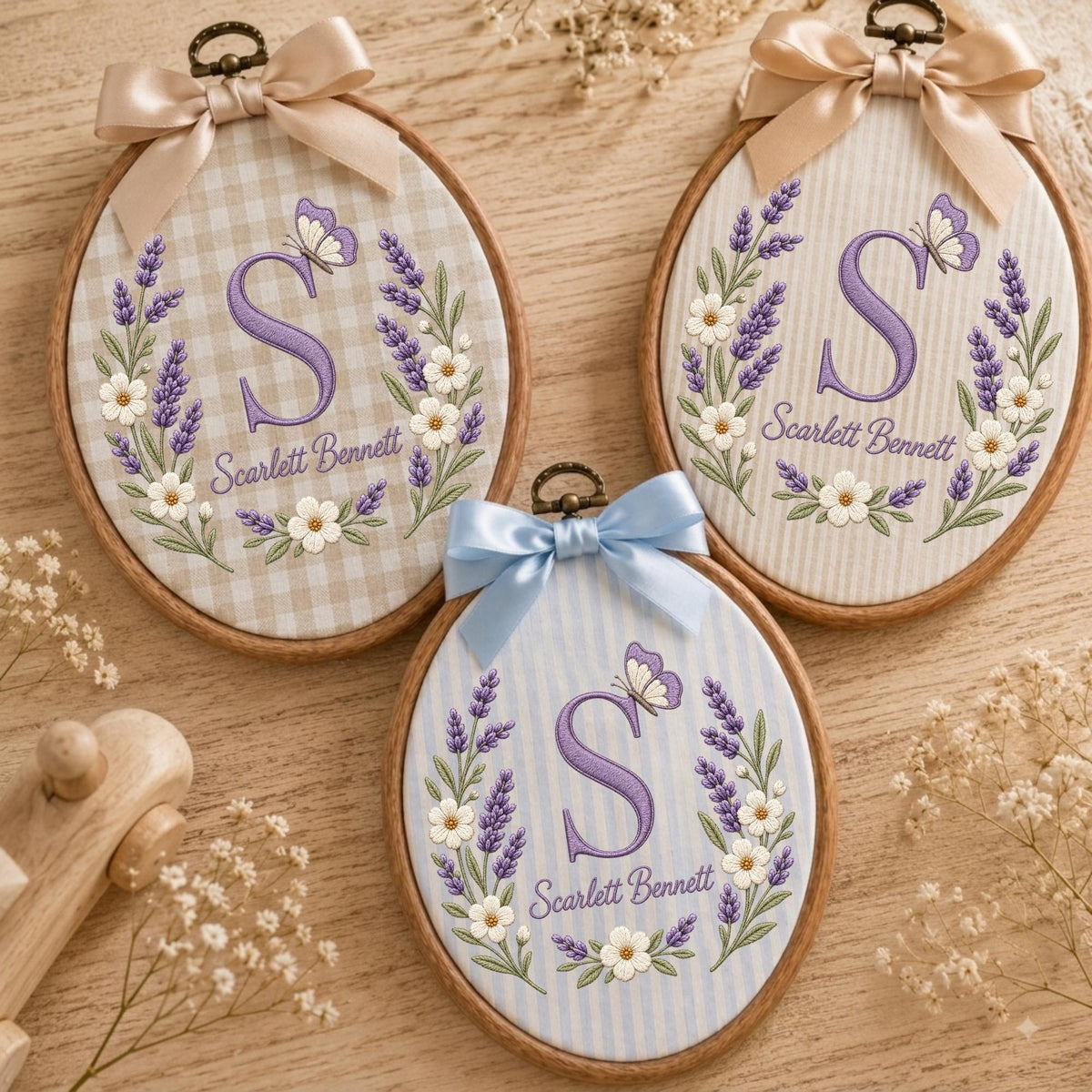 May include: Three oval wooden embroidery hoops featuring fabric backgrounds with lavender and white flower embroidery, a purple letter S, a butterfly, and the name Scarlett Bennett. Each hoop is topped with a decorative satin ribbon bow.