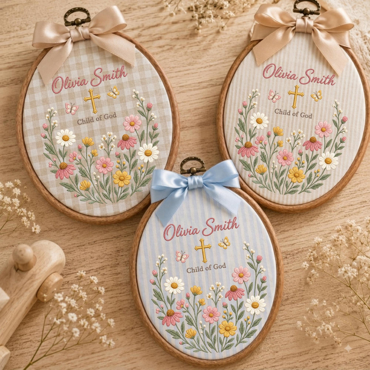 May include: Three oval wooden embroidery hoops featuring fabric backgrounds with gingham or striped patterns. Each hoop displays the embroidered name Olivia Smith, a gold cross, butterflies, and colorful wildflowers with the text Child of God.