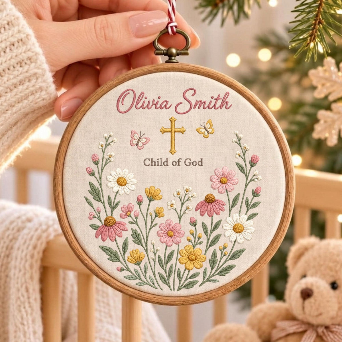 May include: A circular wooden embroidery hoop containing a cream-colored fabric with floral embroidery. The text reads Olivia Smith and Child of God, centered above a gold cross, two butterflies, and a colorful arrangement of daisies and wildflowers.