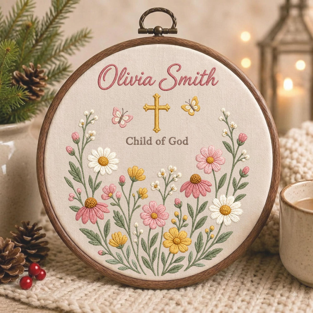 May include: A circular wooden embroidery hoop containing fabric with the embroidered name Olivia Smith, a gold cross, and the text Child of God. The design features colorful flowers in shades of pink, yellow, and white, with two small butterflies.