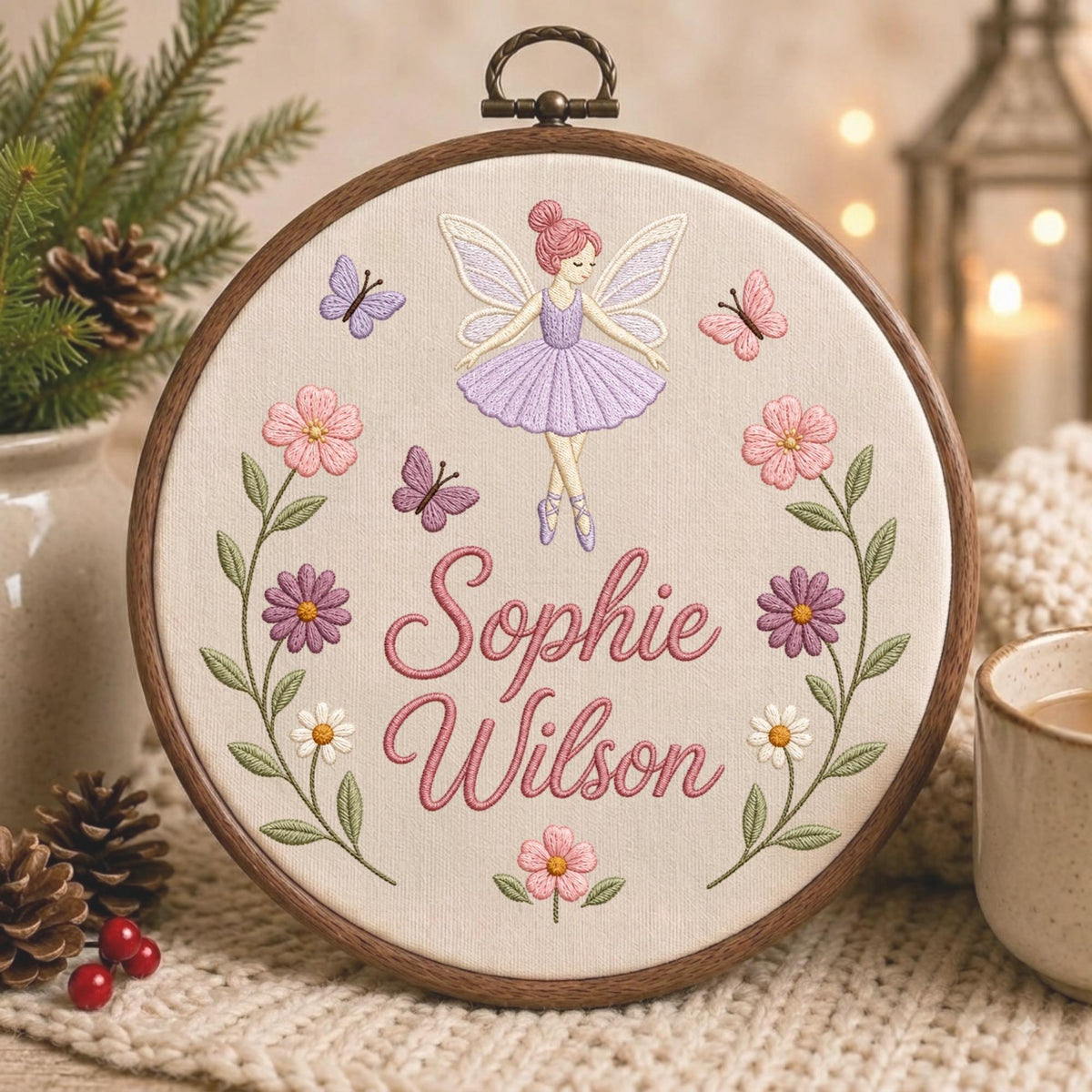 May include: A circular wooden embroidery hoop containing a cream-colored fabric panel. The embroidery features a fairy in a purple dress, butterflies, and flowers surrounding the embroidered text Sophie Wilson in a pink cursive script font.